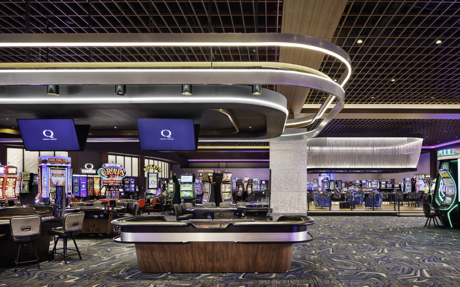 Q Casino gaming floor; dynamic lighting and colorful hues engage playful and high energy in the room; variety of gambling games all around the foreground and background