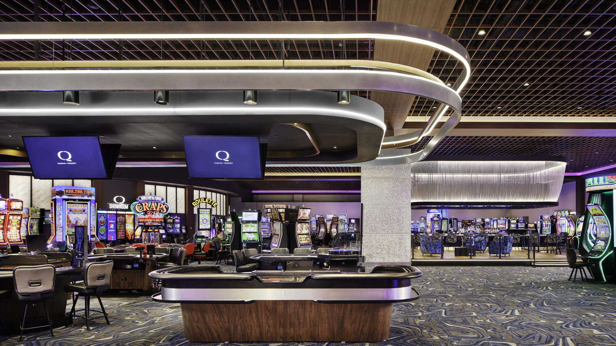 Q Casino gaming floor; dynamic lighting and colorful hues engage playful and high energy in the room; variety of gambling games all around the foreground and background