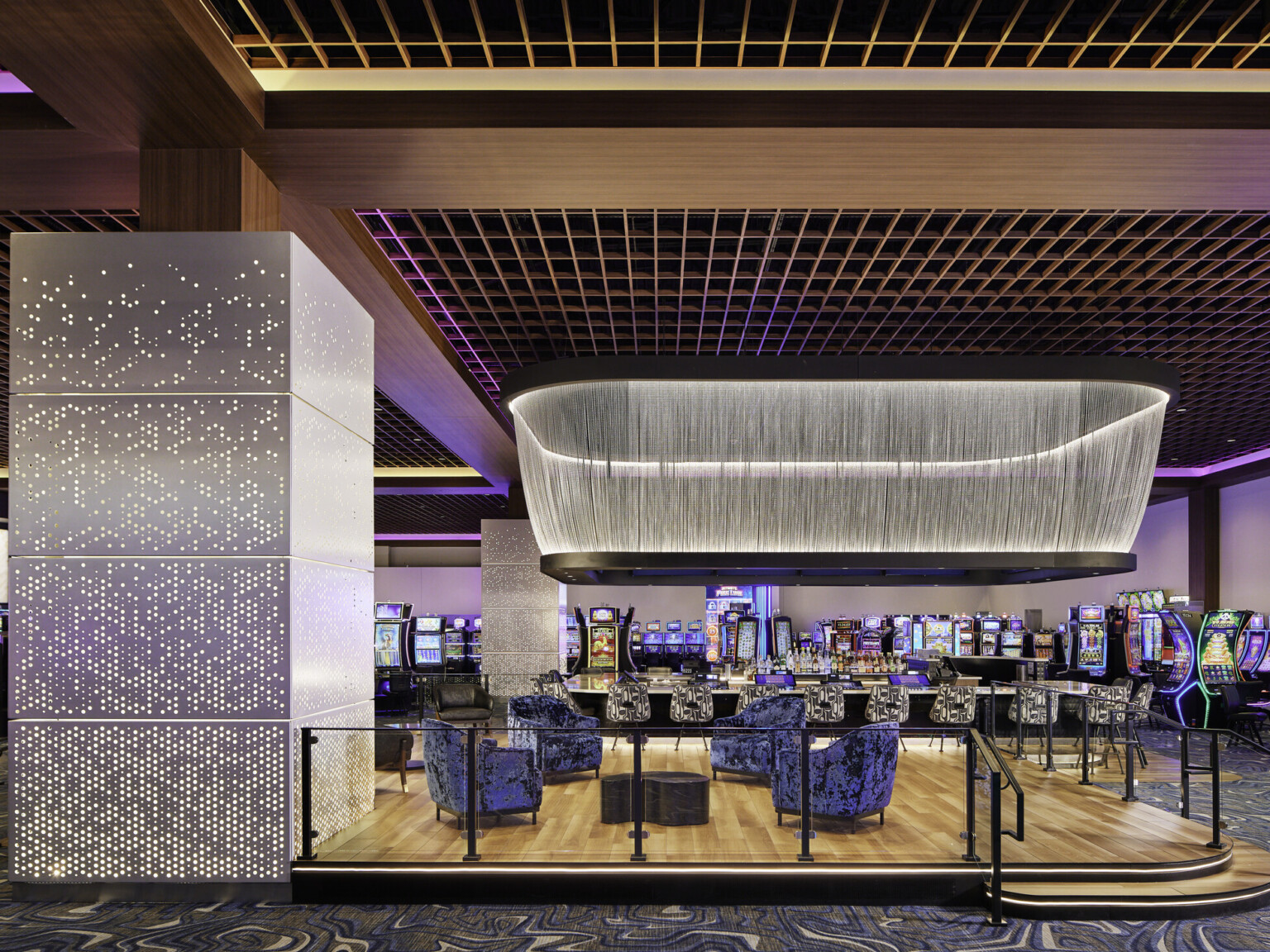 Q Casino designated lounge seating space on the gambling floor overhead intricate lighting feature and bright colored lights surround for ambience; shiny luxurious feel to the space
