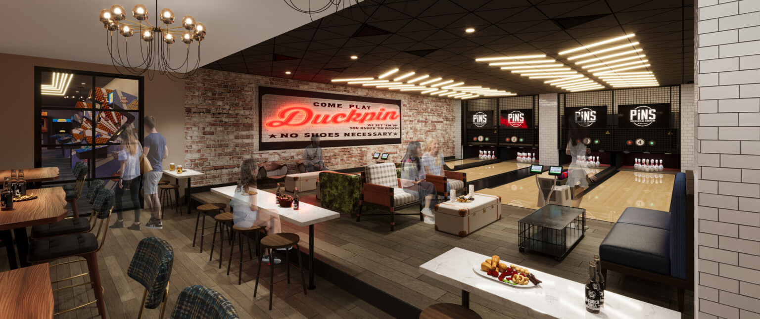 Bowling alley with red neon sign, black couches, tabletop area with wooden chairs.