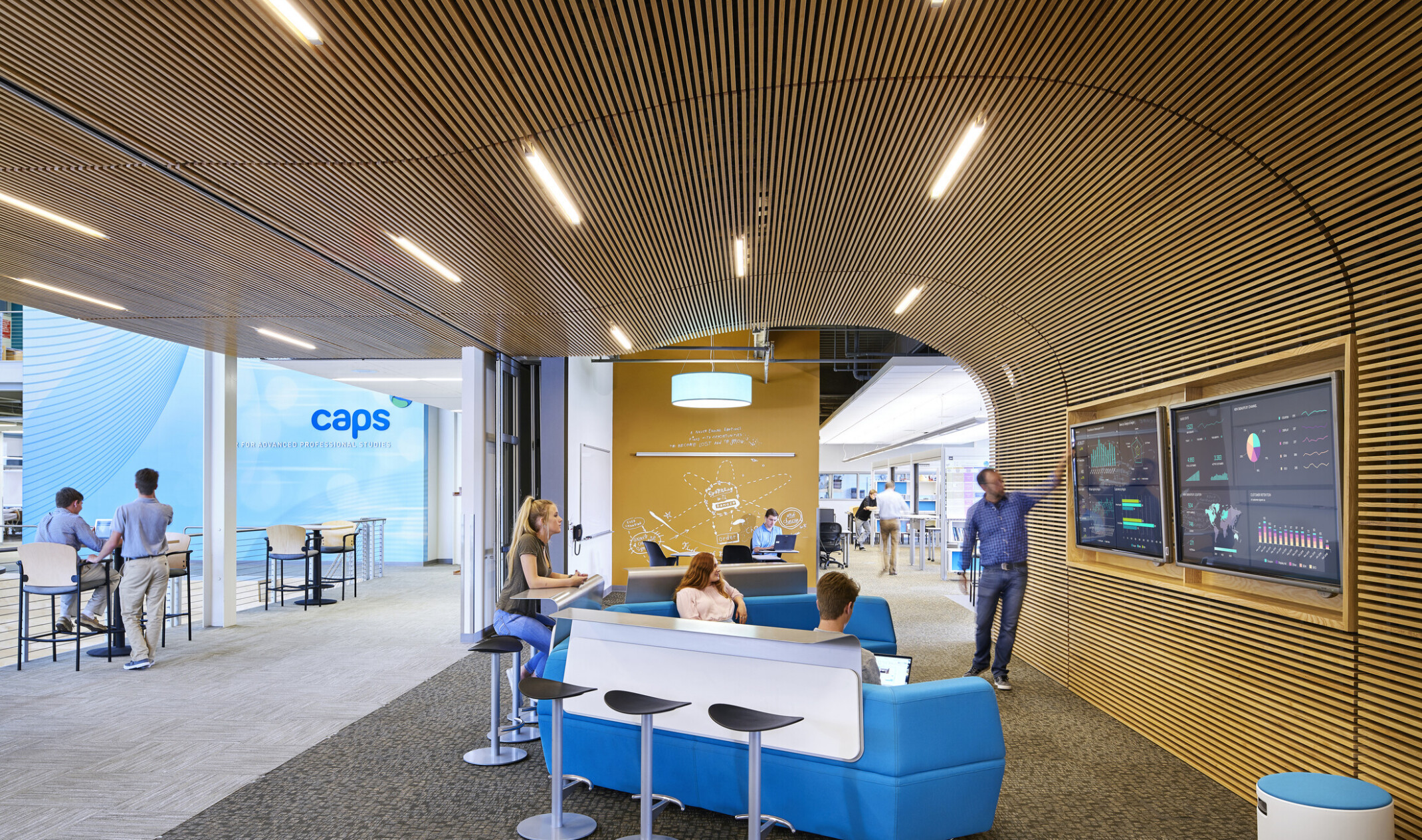 Open concept working space with blue couches, a wooden wall and TV displays