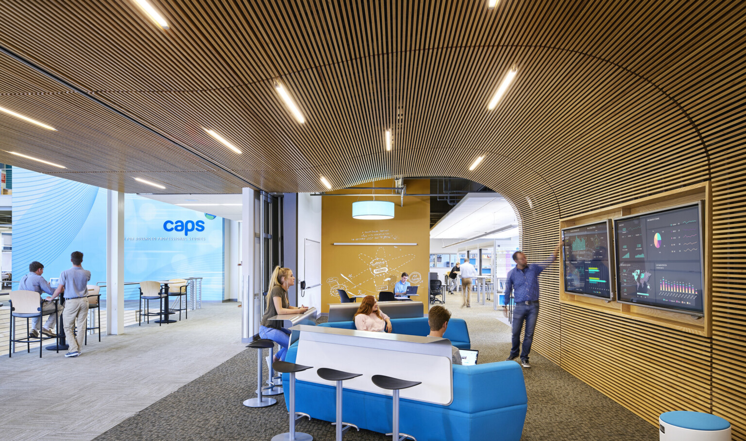 Open concept working space with blue couches, a wooden wall and TV displays