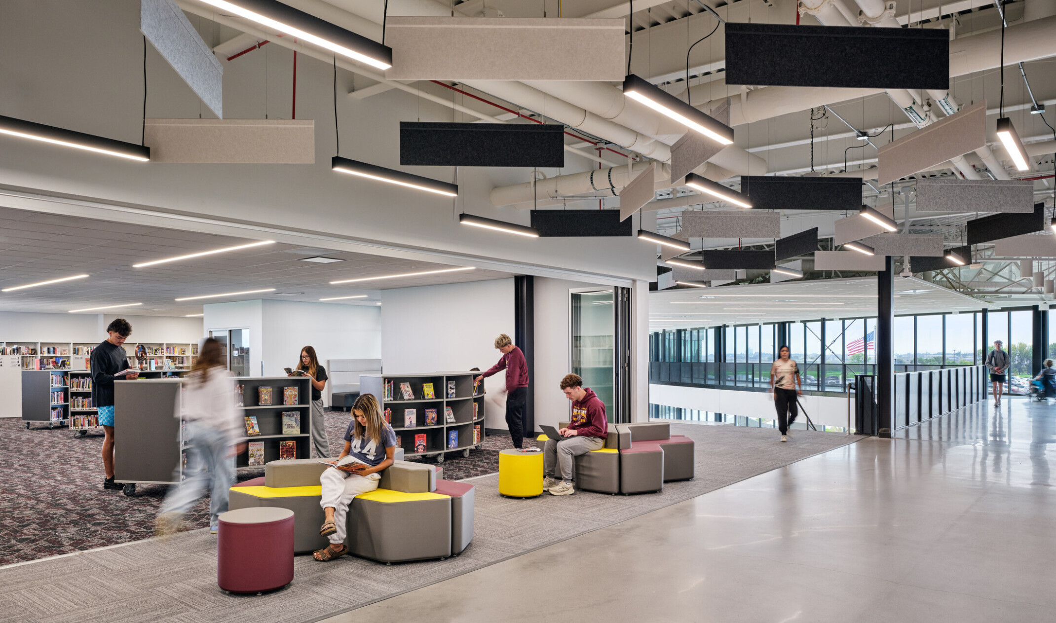 interior of a modern school building library; modern light from background windows lights modular furniture and half height book shelves
