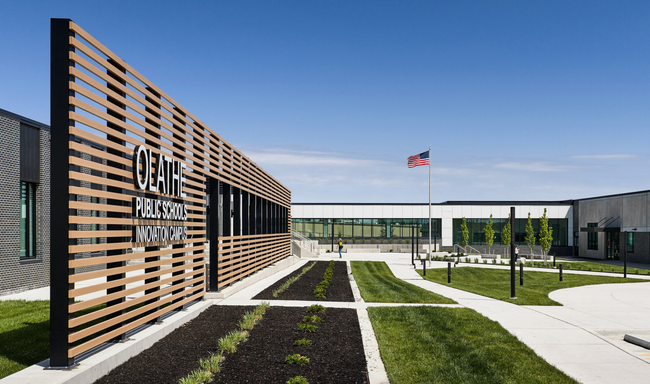 exterior view of Olathe innovation center; large wood-plank facade in front of sidewalks with grass seperations