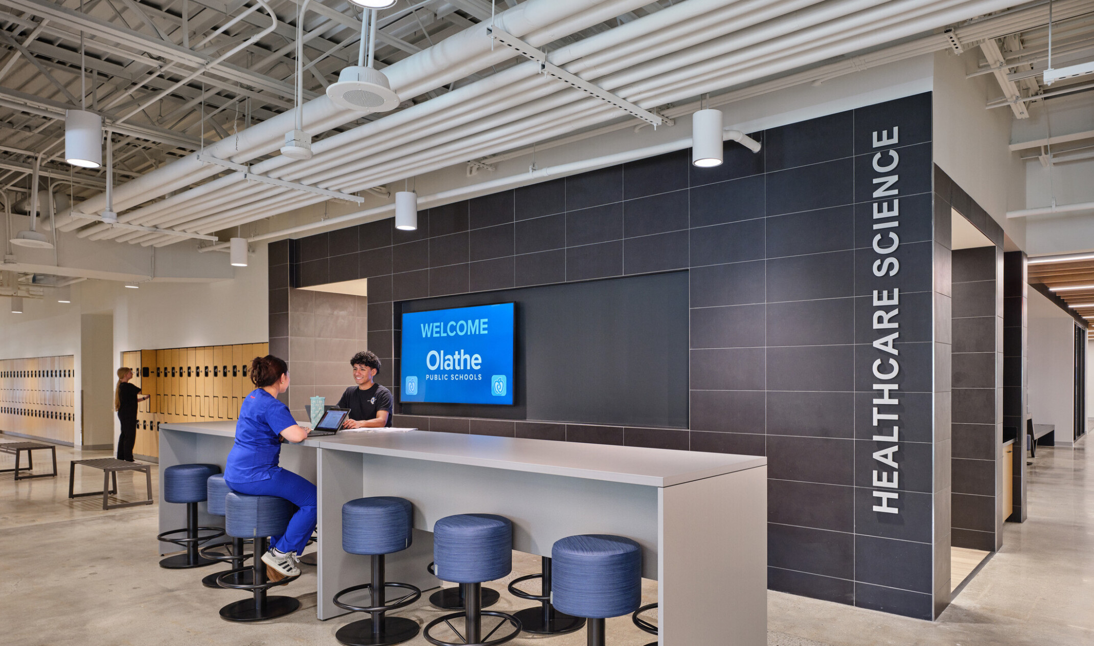 common space in the Olathe innovation center; students sitting at bar-seated hightop on laptops with lockers in the background