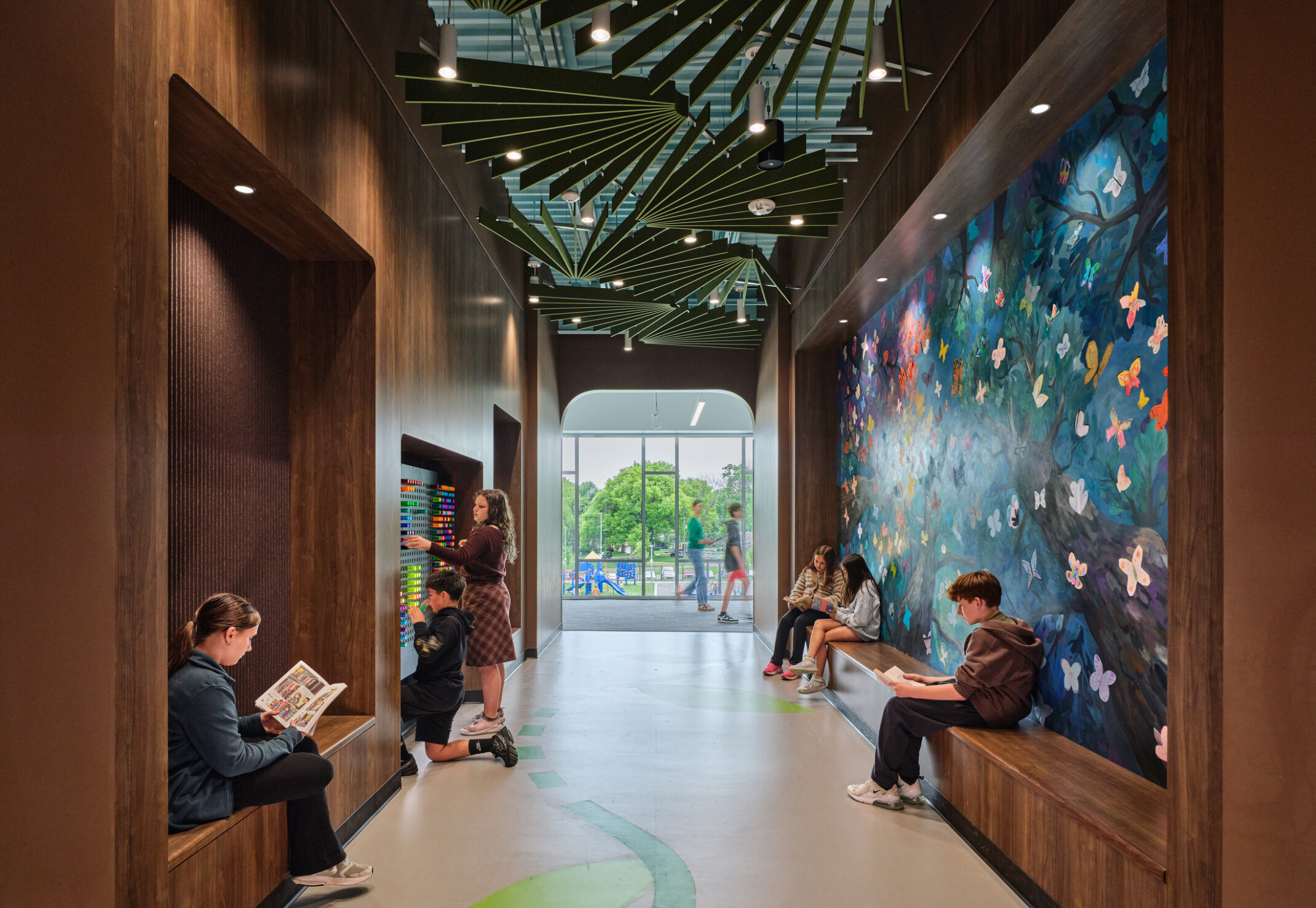Hallway with students collaborating in built in bench seating facing a large set of floor to ceiling windows