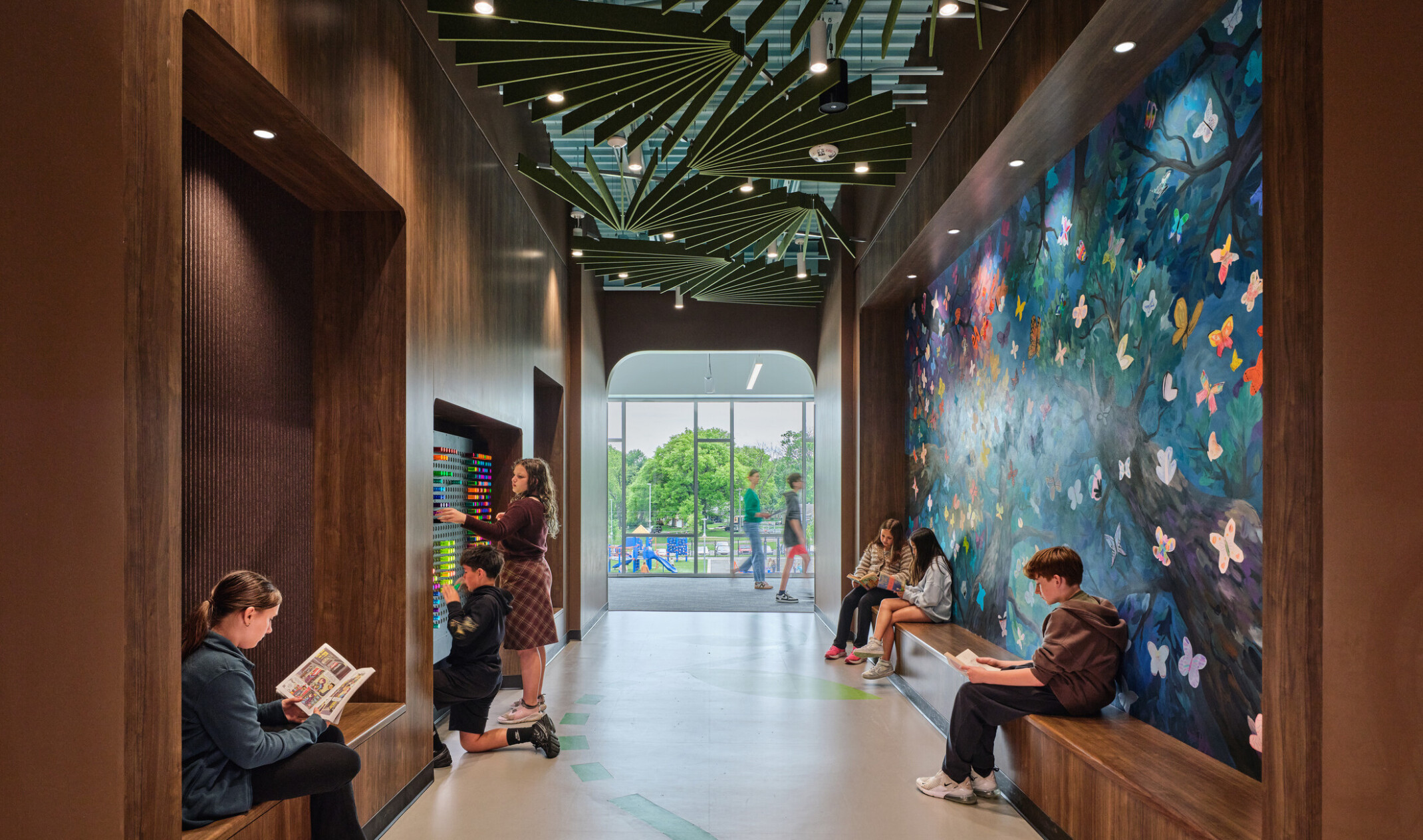 Hallway with students collaborating in built in bench seating facing a large set of floor to ceiling windows