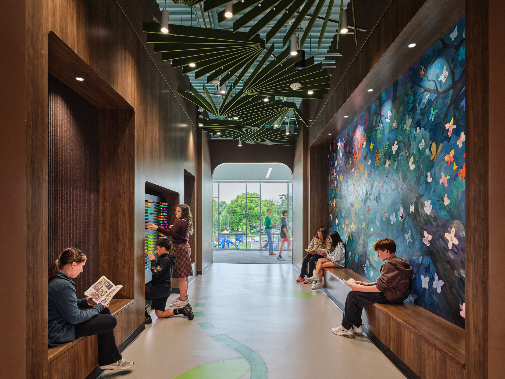 Hallway with students collaborating in built in bench seating facing a large set of floor to ceiling windows