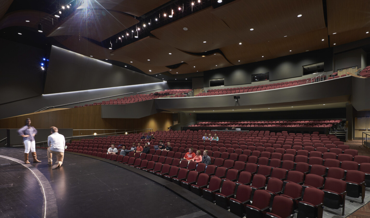 Theater viewed from stage right looking to red theater seats. Black walls with wood accents. Acoustic panels above balcony