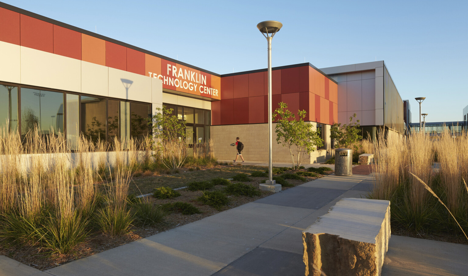 Stone base on 1 story building with orange panels. Building labeled Franklin Technology Center is surrounded by native plants