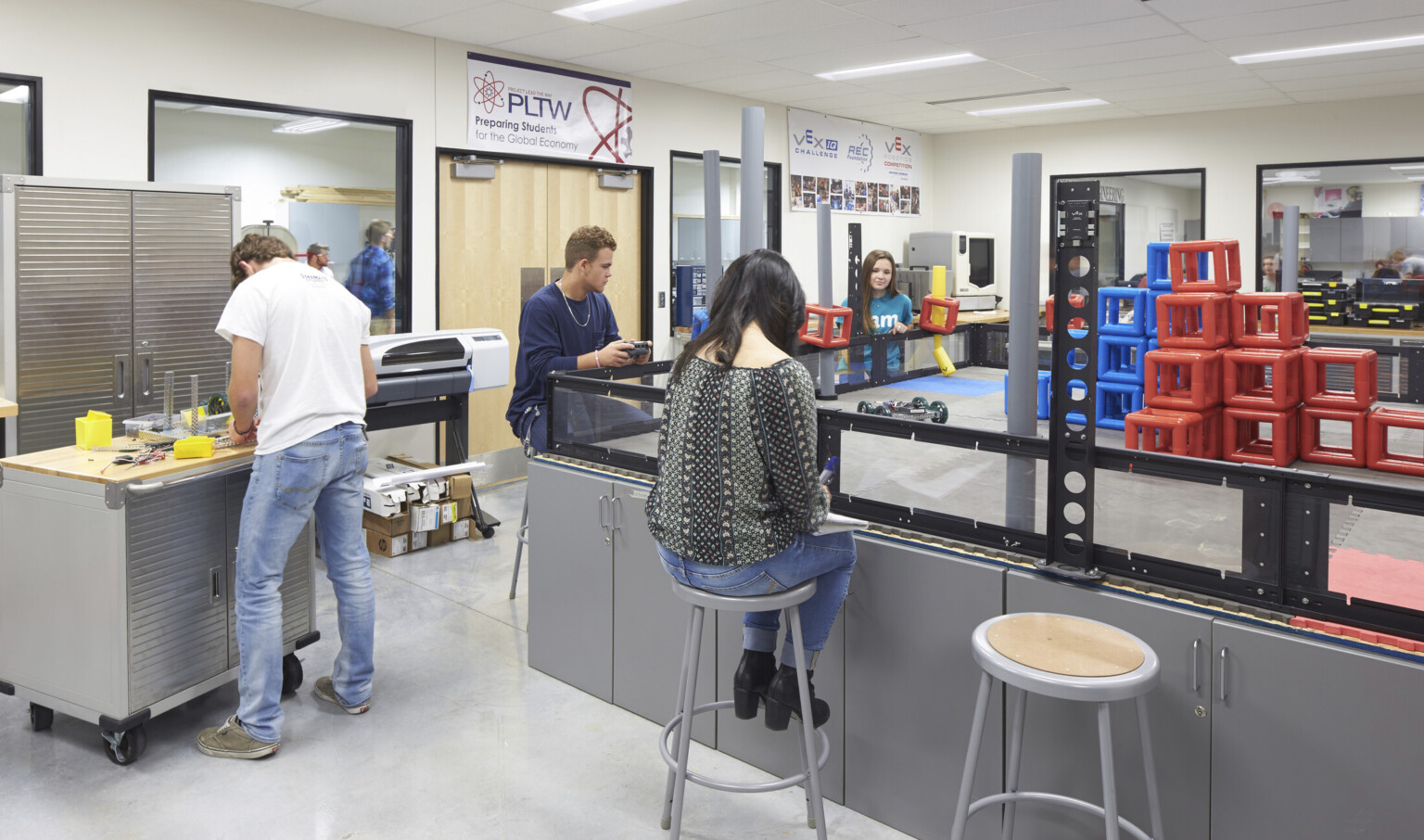 Students work in robotics lab. Large boxed in counter with stools has remote control car and blocks on top.