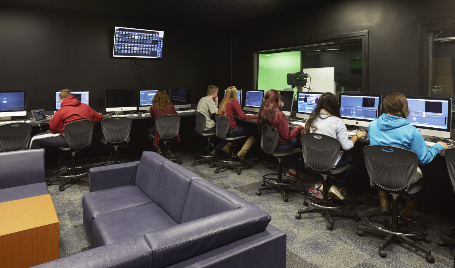 Computers with video editing equipment line 2 walls facing away from couches. Window, right looks to greenscreen and lighting