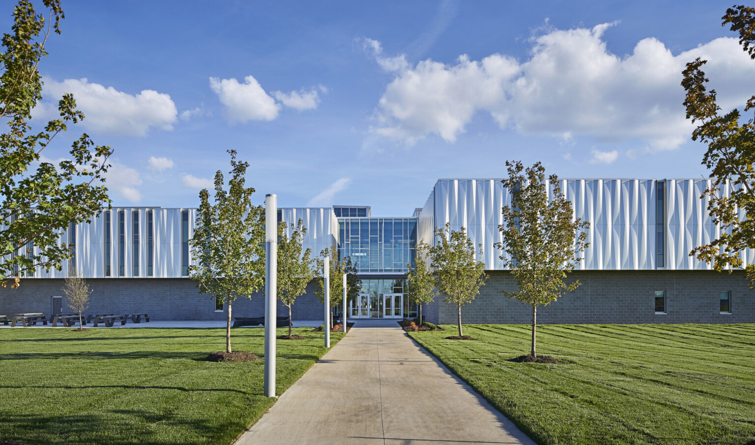 Front view of building looking down a treelined path to the front entrance with 2 sets of glass double doors