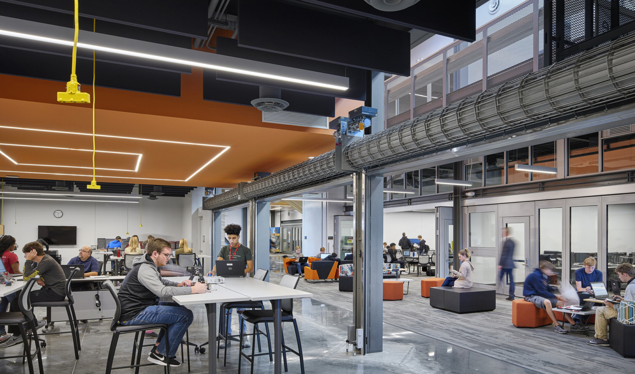 Large commons space with seating under a black ceiling and a geometric orange drop ceiling detail with recessed lights