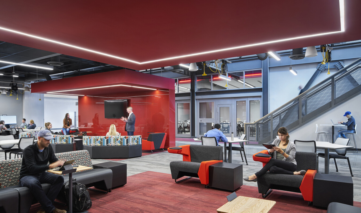 Carpeted seating area. Left, a red partition and illuminated canopy separates a section. A staircase with grey rail is right