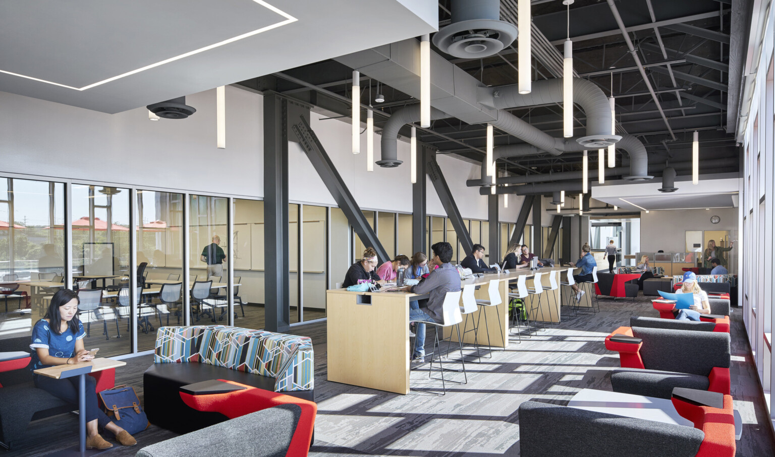 Hallway with seating spaces. Floor to ceiling windows, right, with transparent wall classrooms left, and drop ceiling details