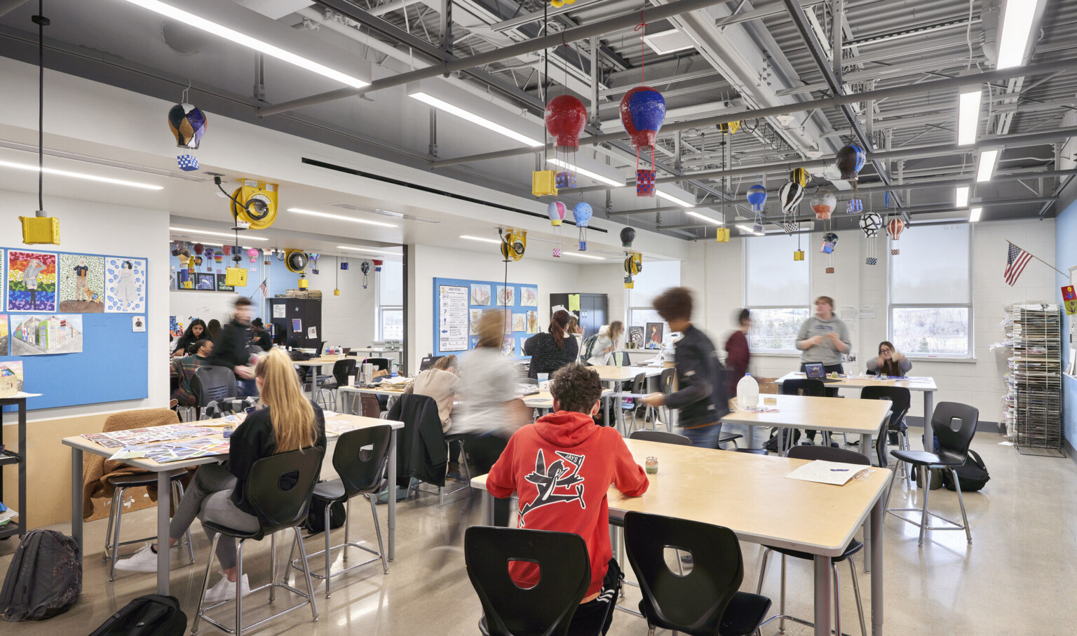 Classroom with exposed structural beams and power cords hanging from ceiling, left. Miniature hot air balloons float above