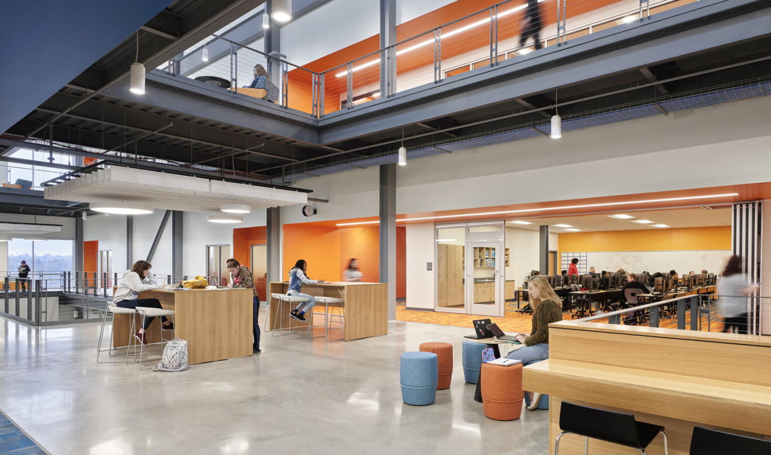 Flexible seating area in hallway with orange accent walls to right. Computer lab with opened flexible wall to hallway