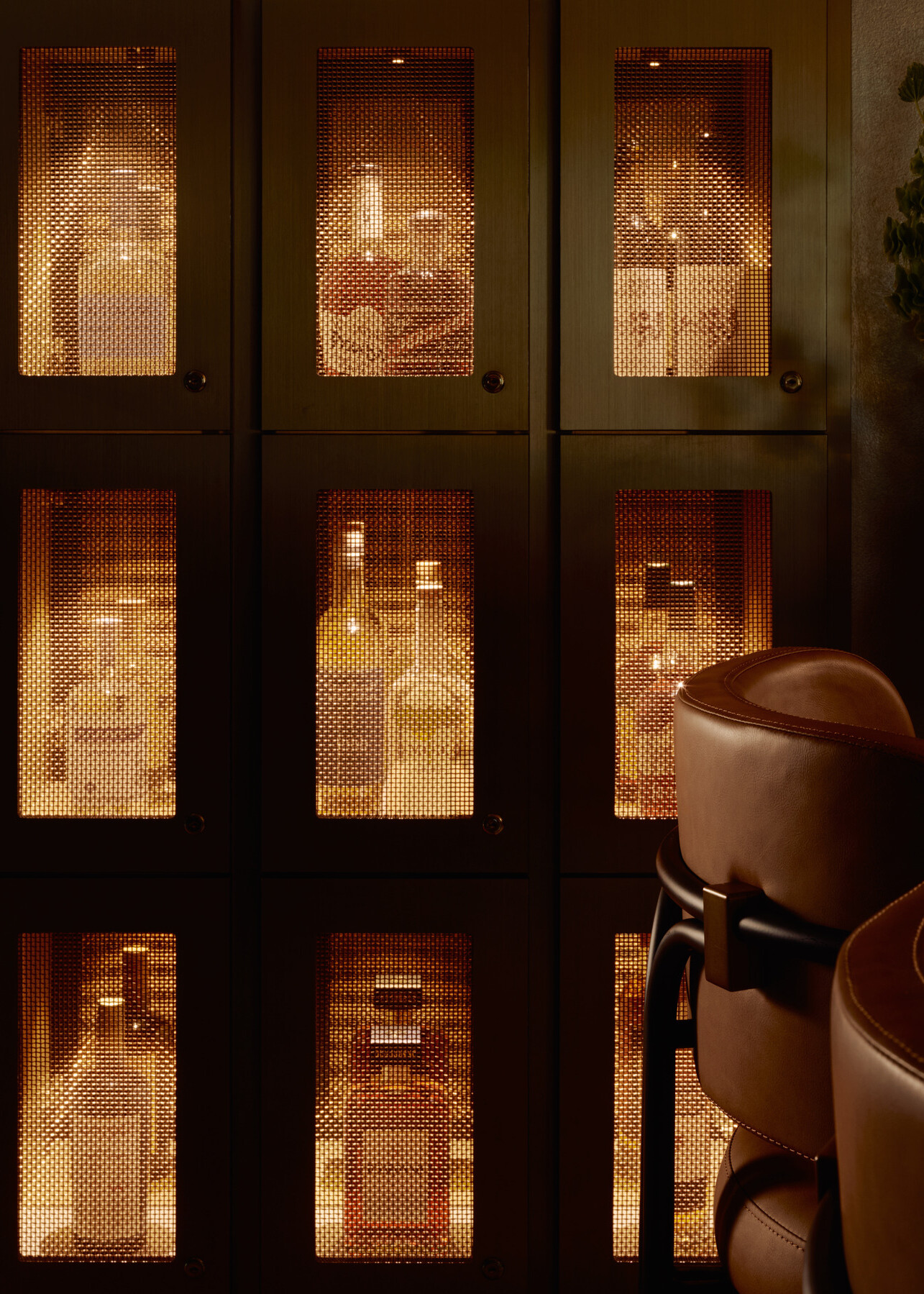 Illuminated members’ bottle lockers at Momentum KC featuring mirrored backing, integrated lighting, and mesh metal fronts that create depth and a subtle glow.