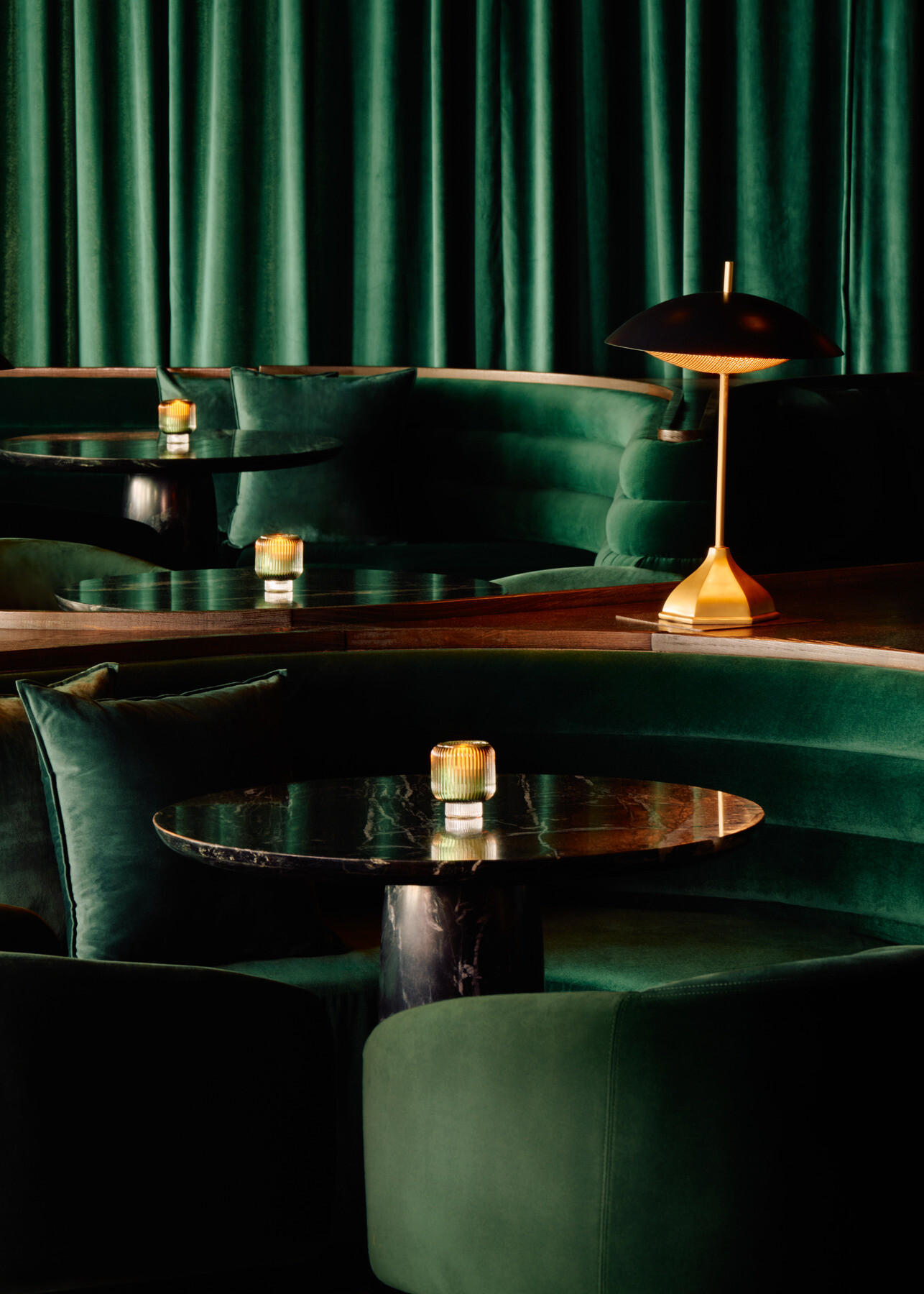 Main lounge at Momentum KC featuring lush green upholstered walls and seating, warm wood bench detailing, and softly illuminated tables creating an intimate atmosphere.