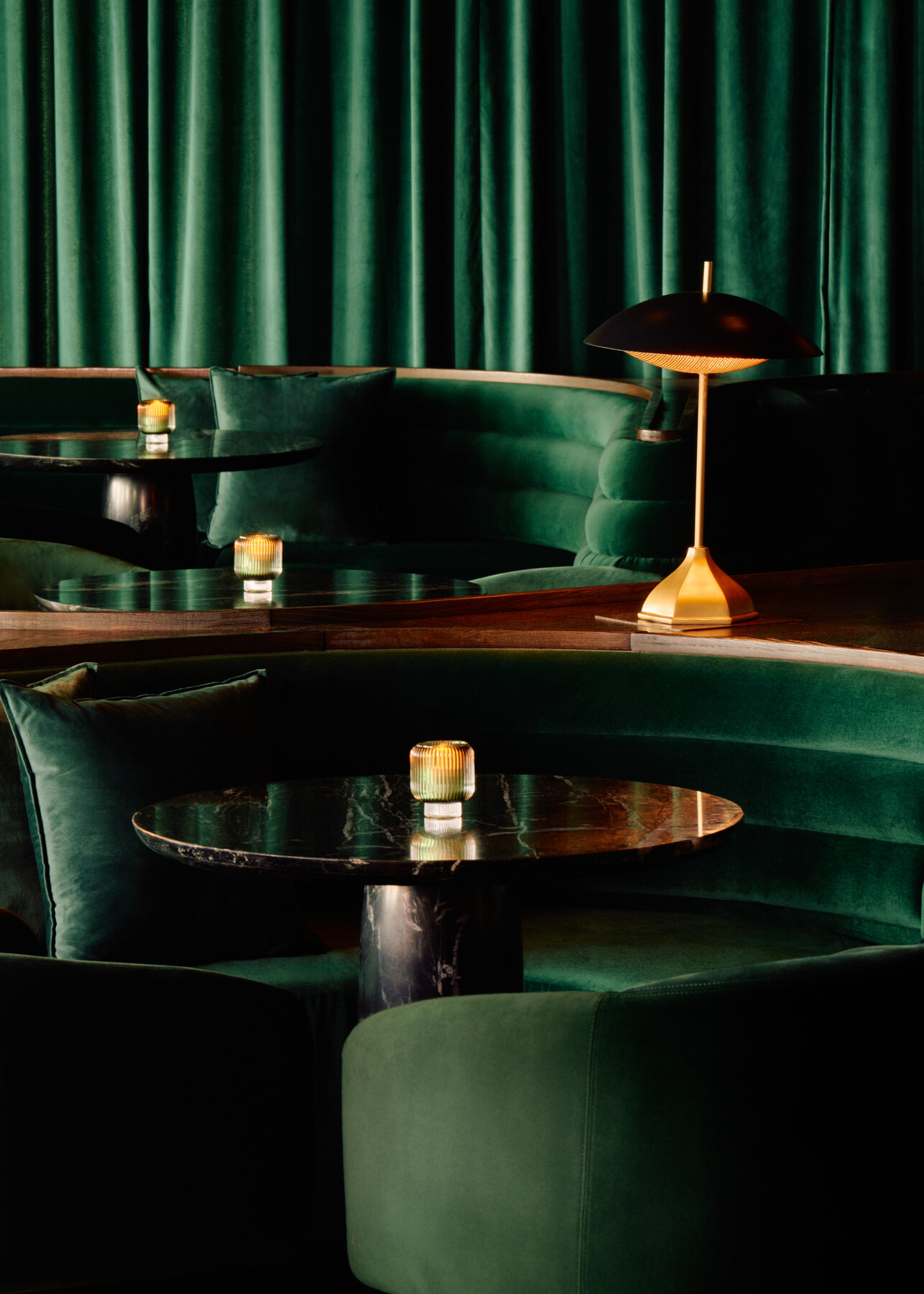 Main lounge at Momentum KC featuring lush green upholstered walls and seating, warm wood bench detailing, and softly illuminated tables creating an intimate atmosphere.