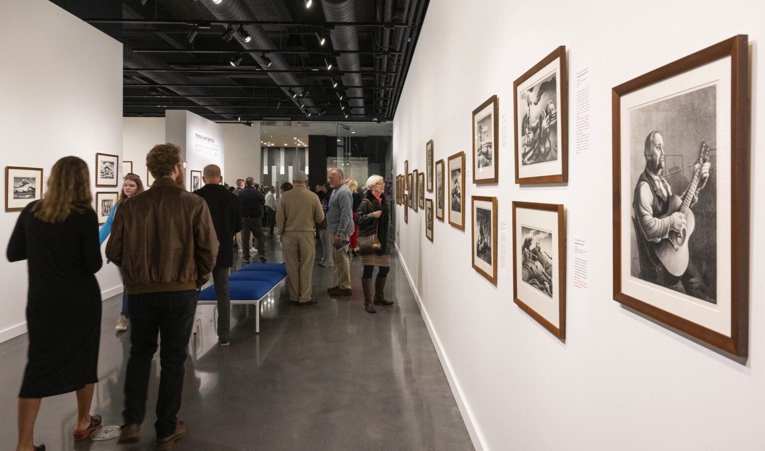 People observing art in an art gallery with white walls and black ceiling, walls are filled with photographs