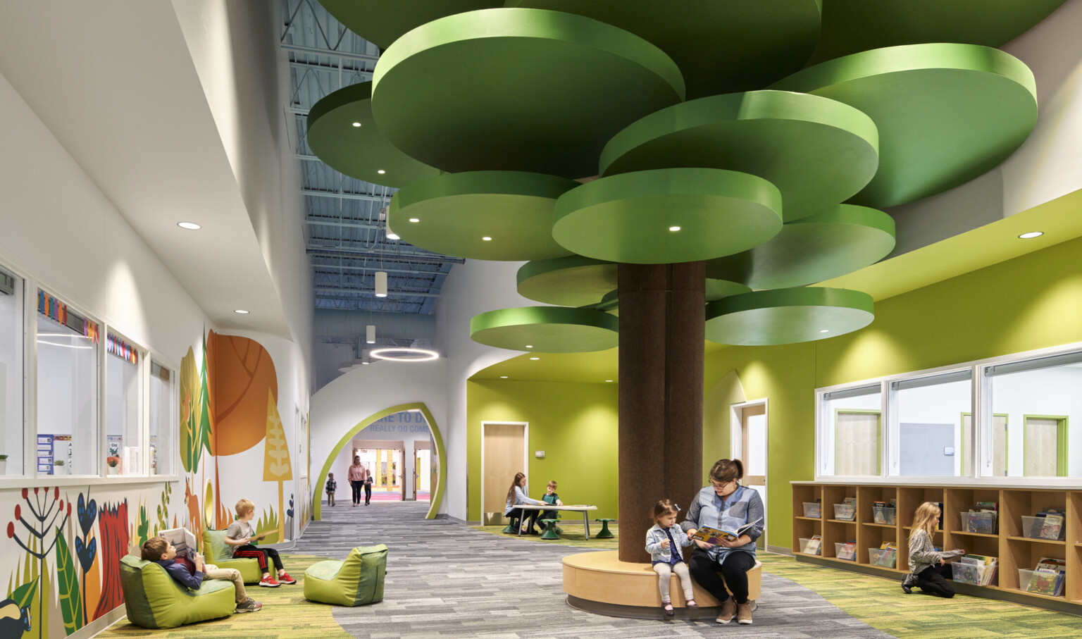 people reading on a brown circular bench with a brown column and green ceiling fixtures in hallway lined with forest graphics