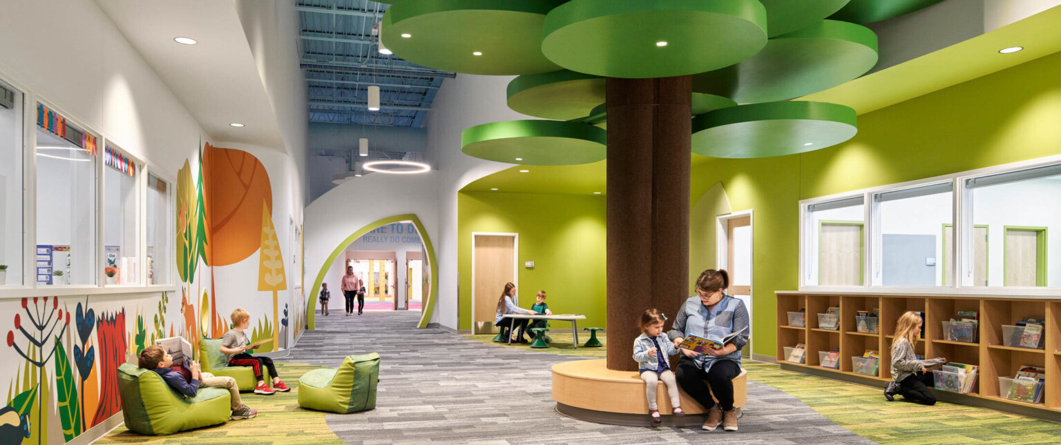 people reading on a brown circular bench with a brown column and green ceiling fixtures in hallway lined with forest graphics