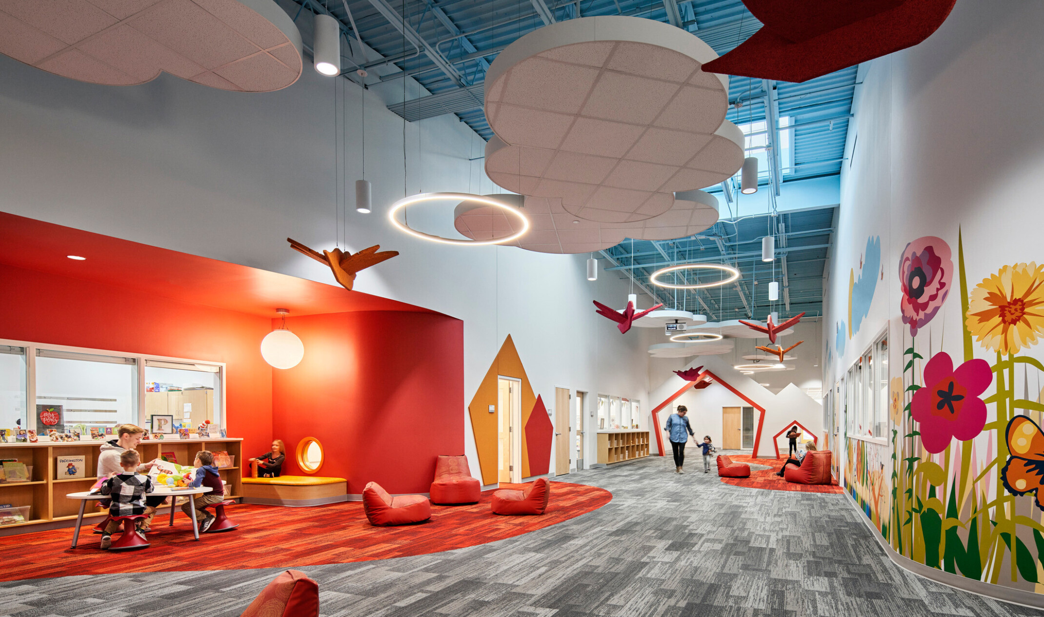 high blue ceilings and grey geometric print carpet with suspended cloud and orange bird elements, bright orange accent wall, mural with brightly colored flowers
