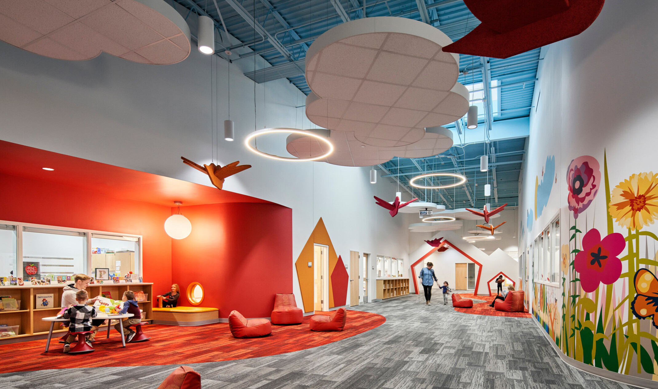 high blue ceilings and grey geometric print carpet with suspended cloud and orange bird elements, bright orange accent wall, mural with brightly colored flowers