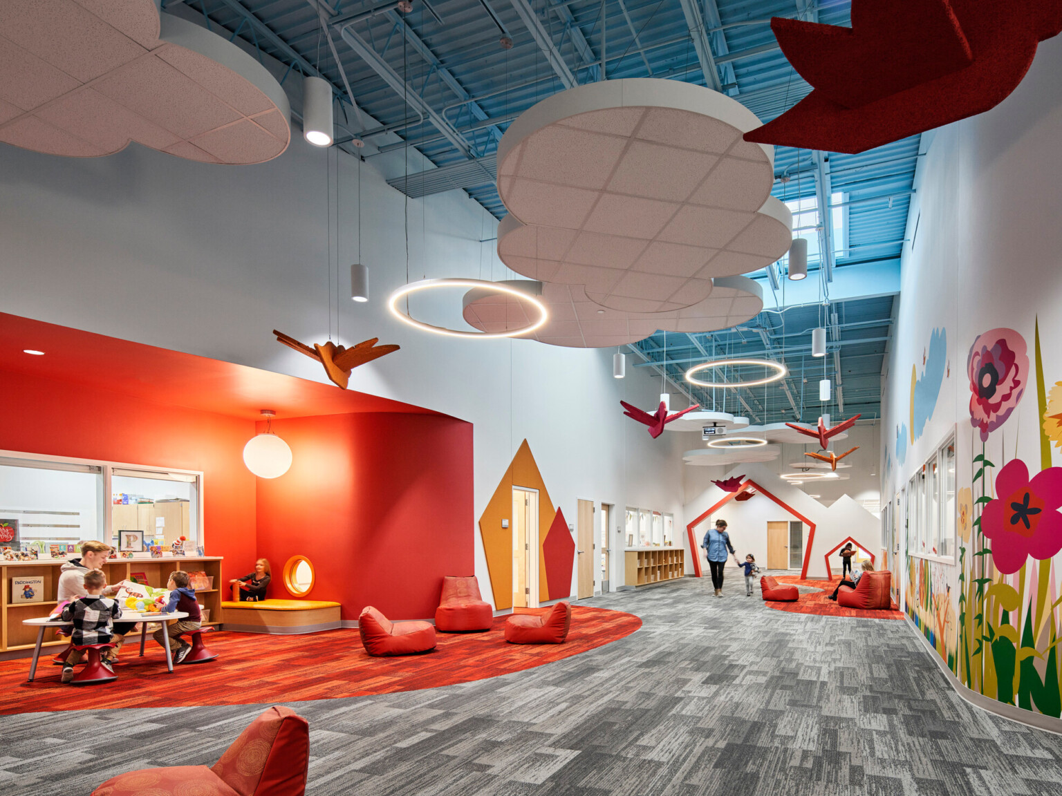 high blue ceilings and grey geometric print carpet with suspended cloud and orange bird elements, bright orange accent wall, mural with brightly colored flowers