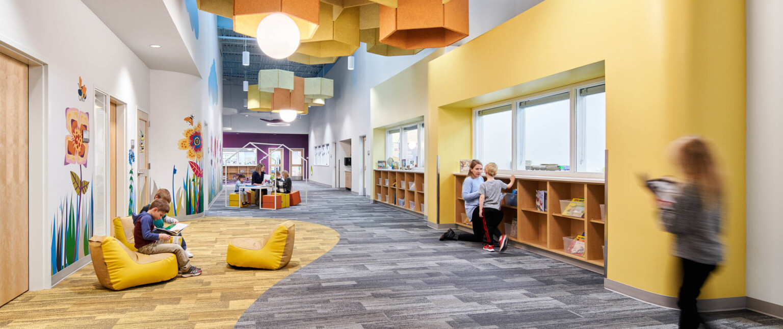 Hallway with comfortable soft seating, yellow wall and carpet accents. Yellow pentagonal baffles and globe pendant lights