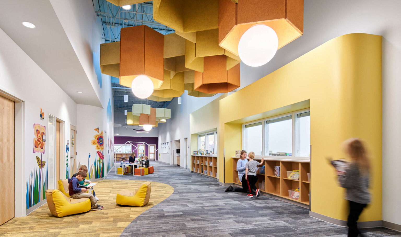 Hallway with comfortable soft seating, yellow wall and carpet accents. Yellow pentagonal baffles and globe pendant lights