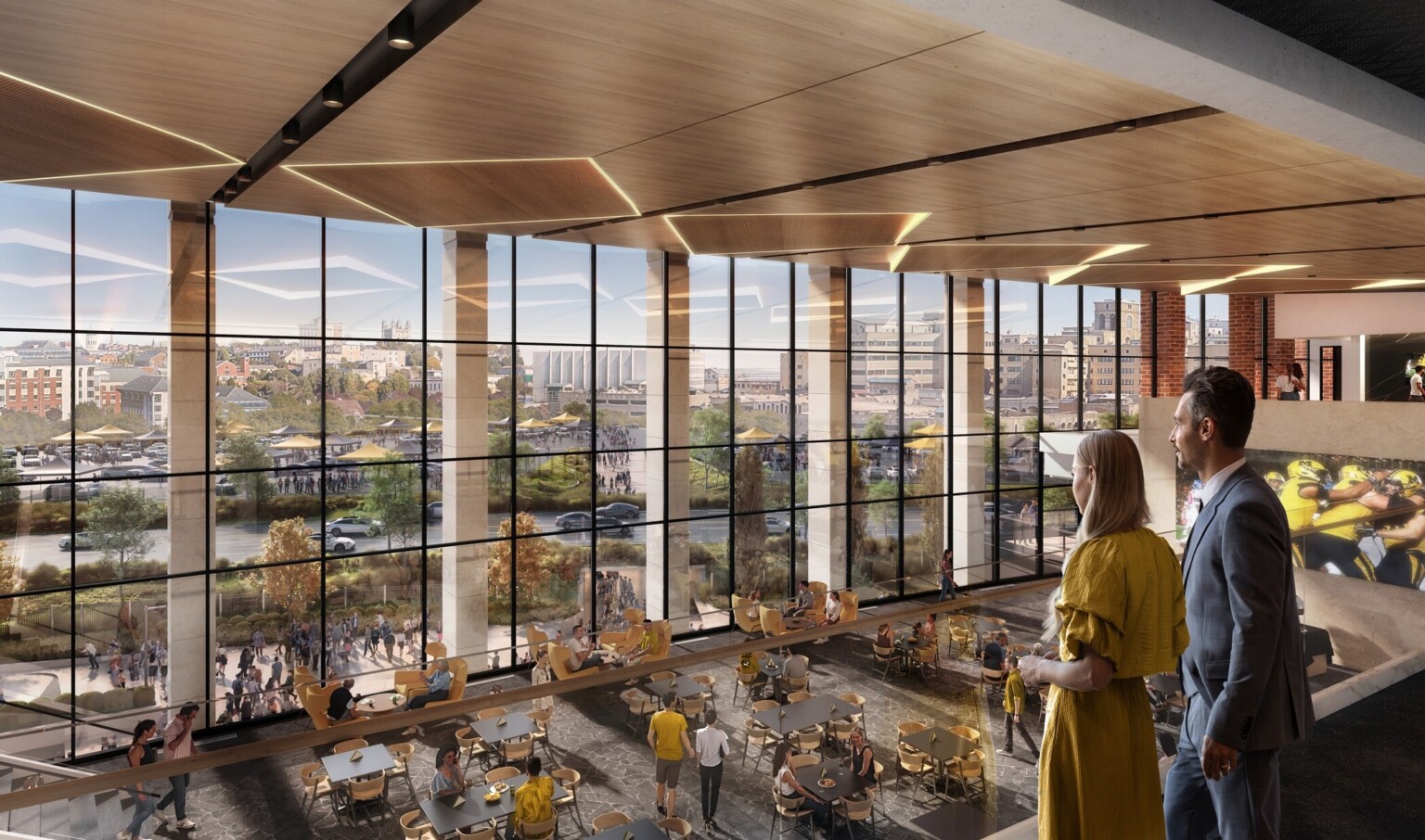Couple standing on a second floor balcony overlooking the first floor filled with tables and chairs in front of large floor to ceiling windows Couple standing on a second floor balcony overlooking the first floor filled with tables and chairs in front of large floor to ceiling windows