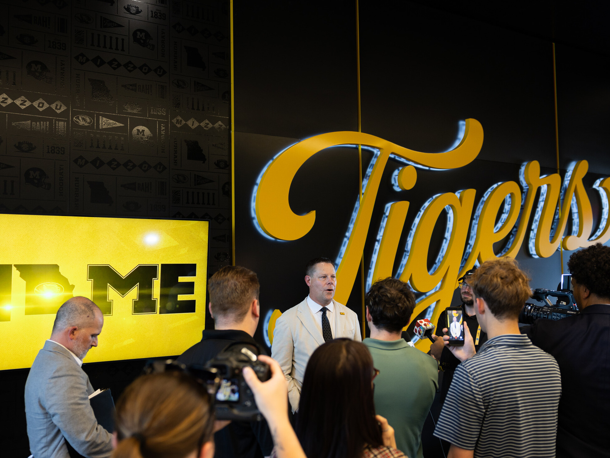 people gathered in University of Missouri Memorial Stadium club facing a yellow sign "Tigers"