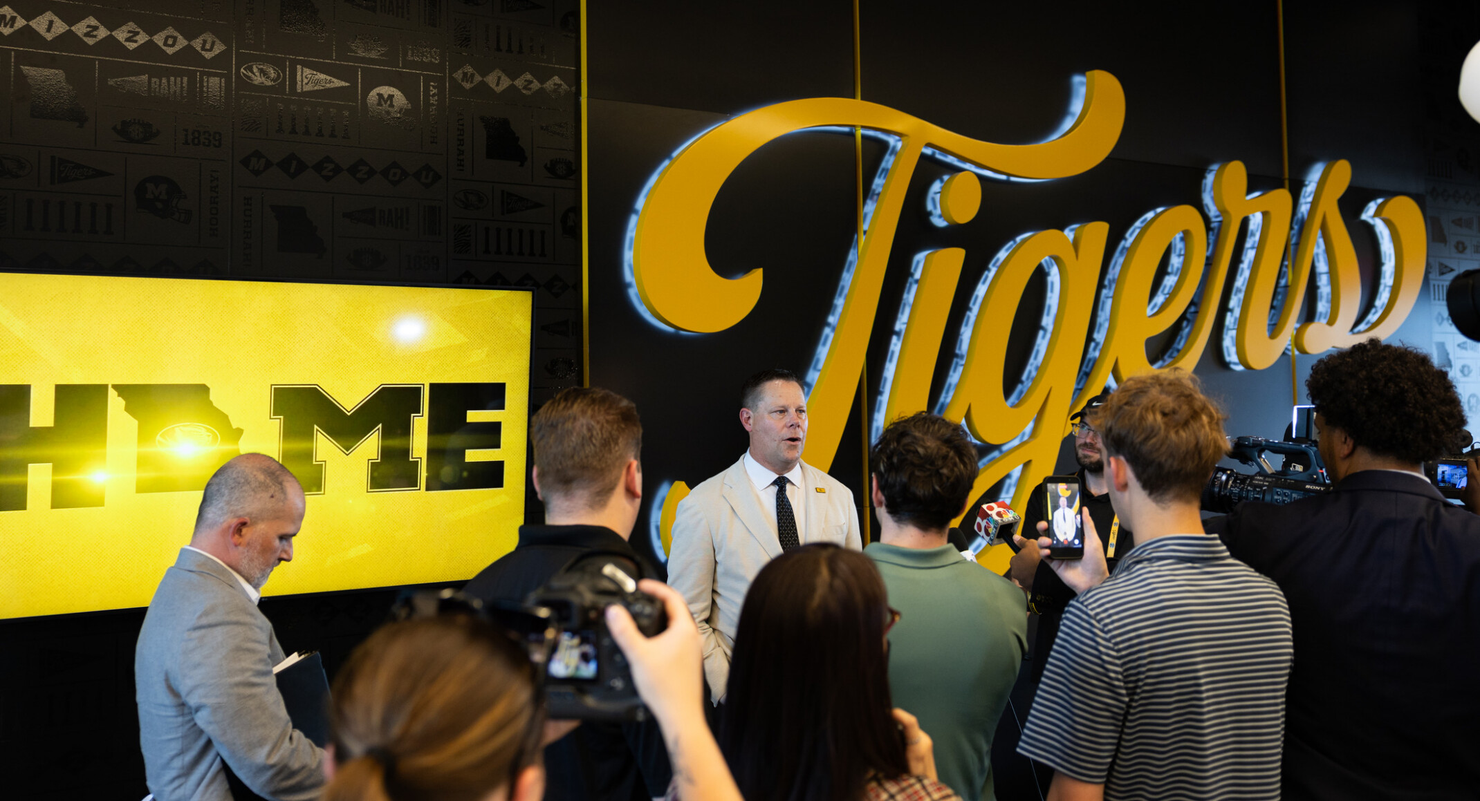 people gathered in University of Missouri Memorial Stadium club facing a yellow sign "Tigers"