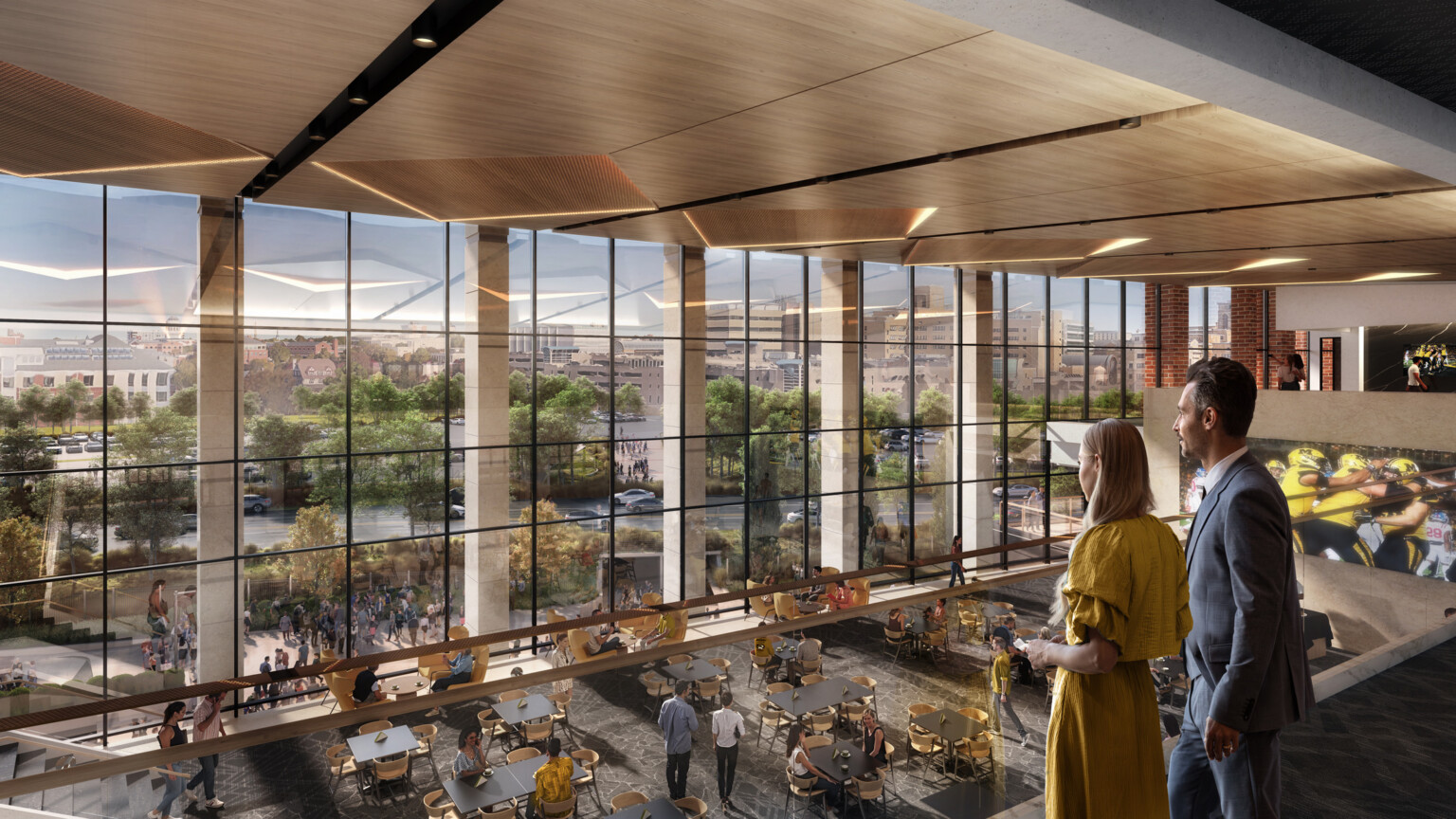 Couple standing on a second floor balcony overlooking the first floor filled with tables and chairs in front of large floor to ceiling windows Couple standing on a second floor balcony overlooking the first floor filled with tables and chairs in front of large floor to ceiling windows