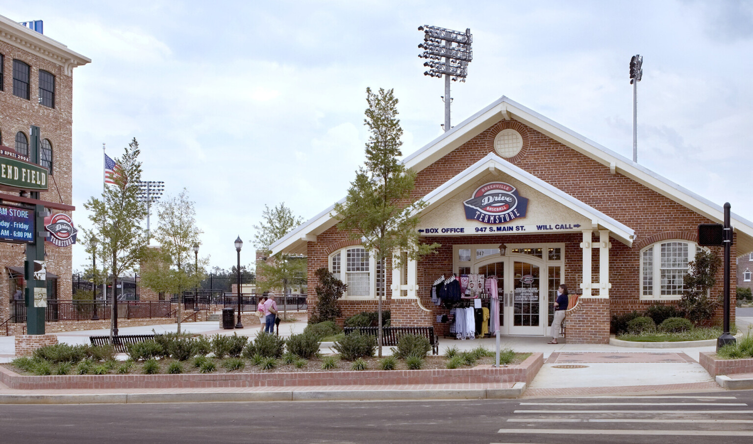 Brick building with pointed roof and entry canopy house team store in stadium plaza with benches and greenery