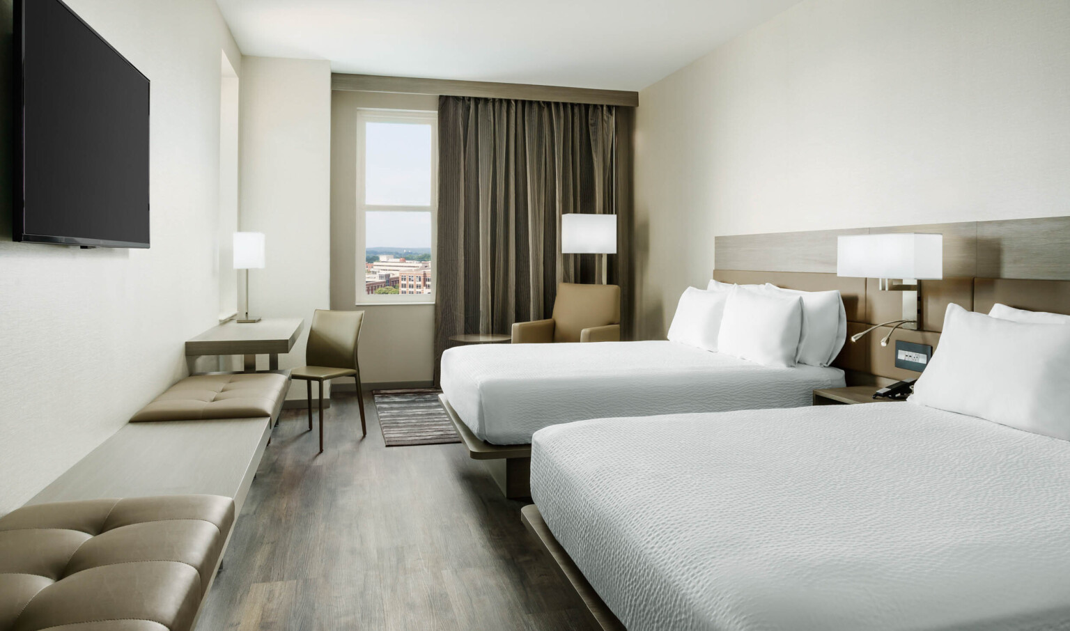 Guest room with two white beds divided by an end table and light fixture. Arm chair by window, all face bench along left wall