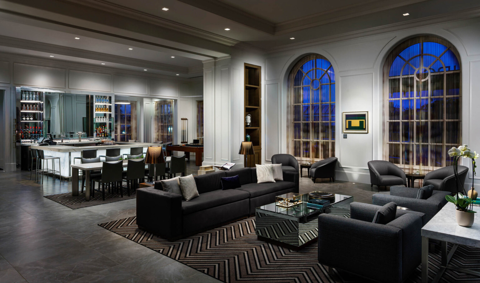 Seating area and arched windows in the evening, in front of bar and table. Pool table by windows in the back.