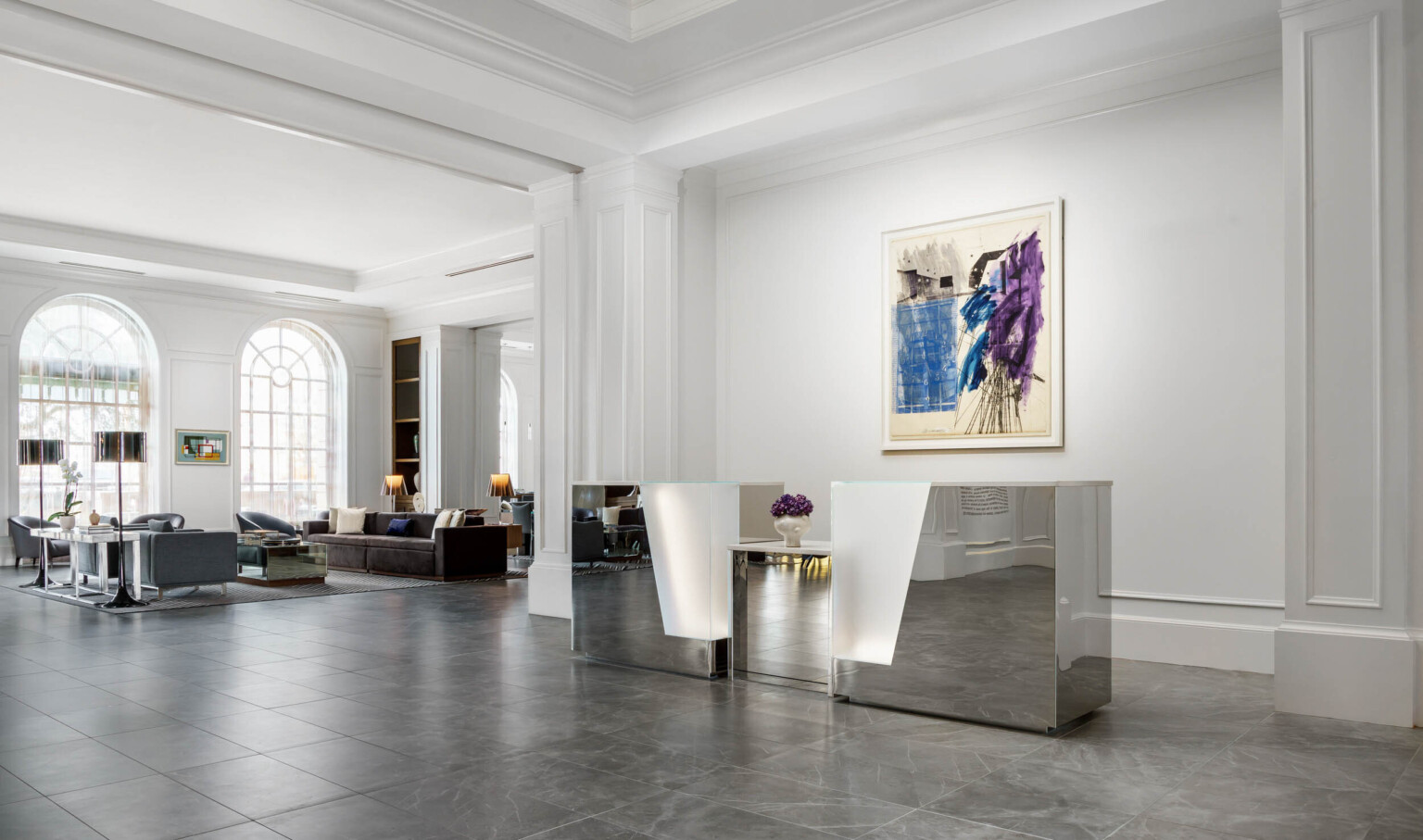 Metallic reception desk with illuminated detail in white AC Hotel Spartanburg lobby with large arch window, seating area left