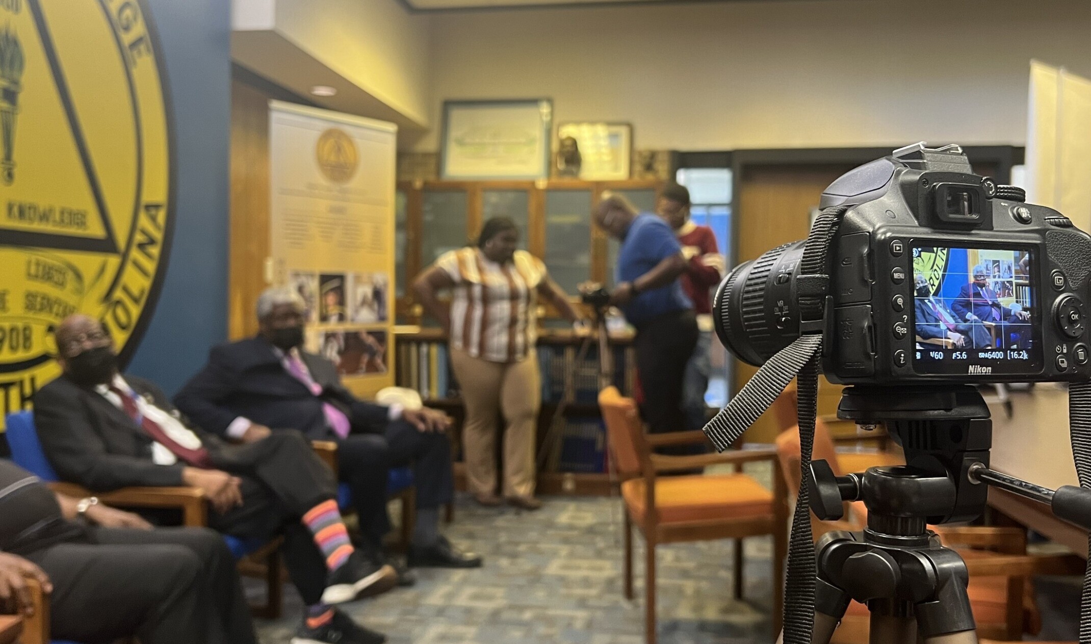Right, forefront camera focused on four individuals sitting against a wall
