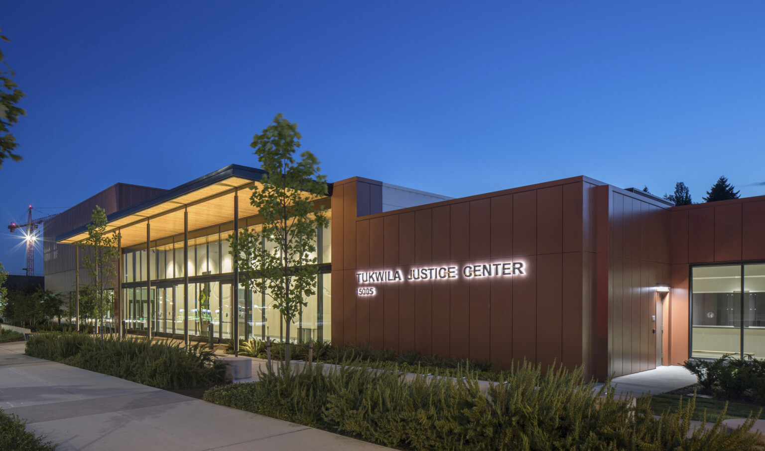 City of Tukwila Justice Center in the evening, with landscaping in the foreground. Single story double height glass facade building