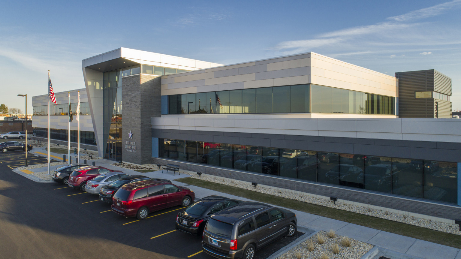 Will County Sheriff's Office, a grey and white 2 story public safety building with large windows and cars in parking lot