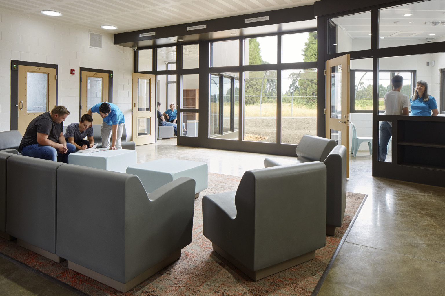 seating area inside Oregon Youth Authority MacLaren Campus with people gathered around grey lounge chairs