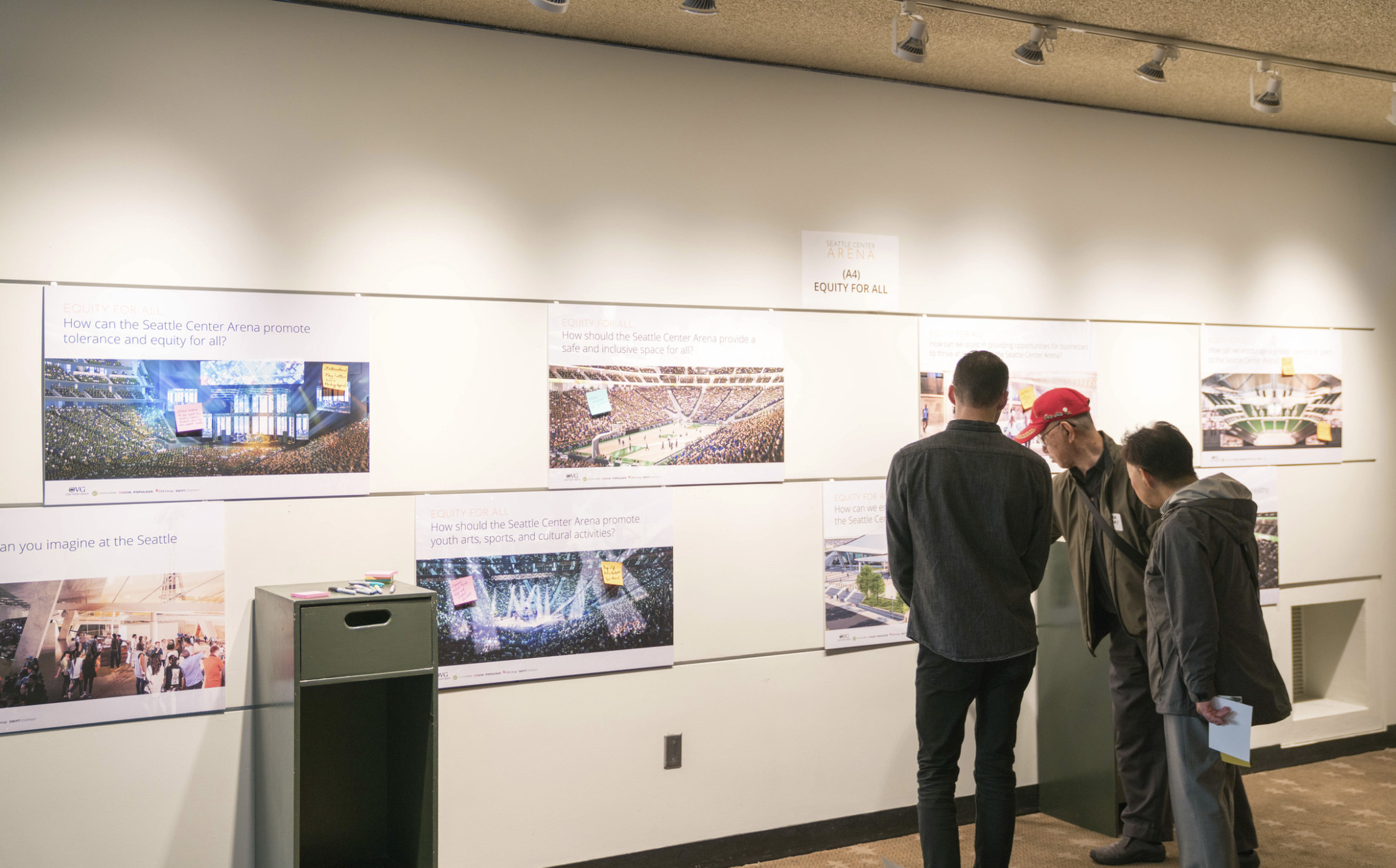 Three men pointing at a photo on white gallery wall in Seattle