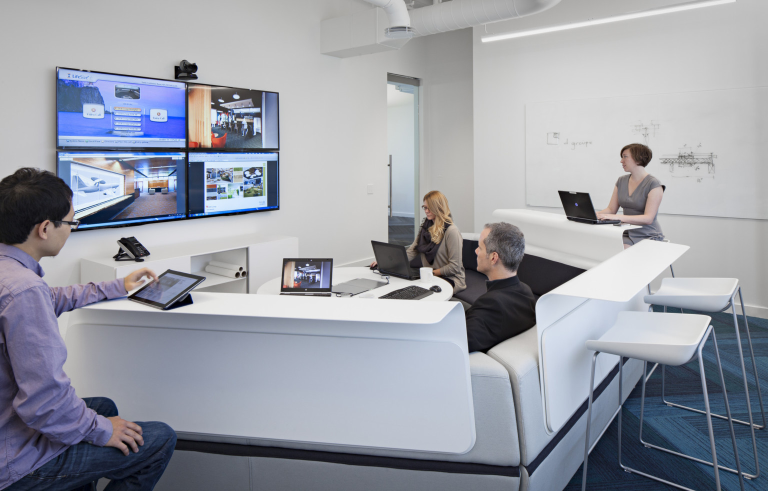 team collaborating with multiple screens, technology, and tiered seating in white conference room