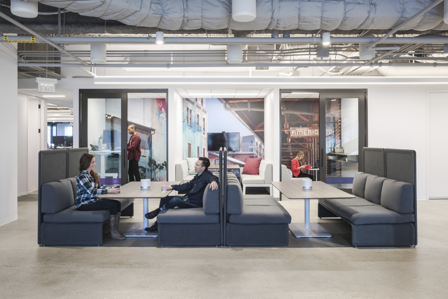 people working at booths with private phone booths behind with transparent walls and large graphic murals