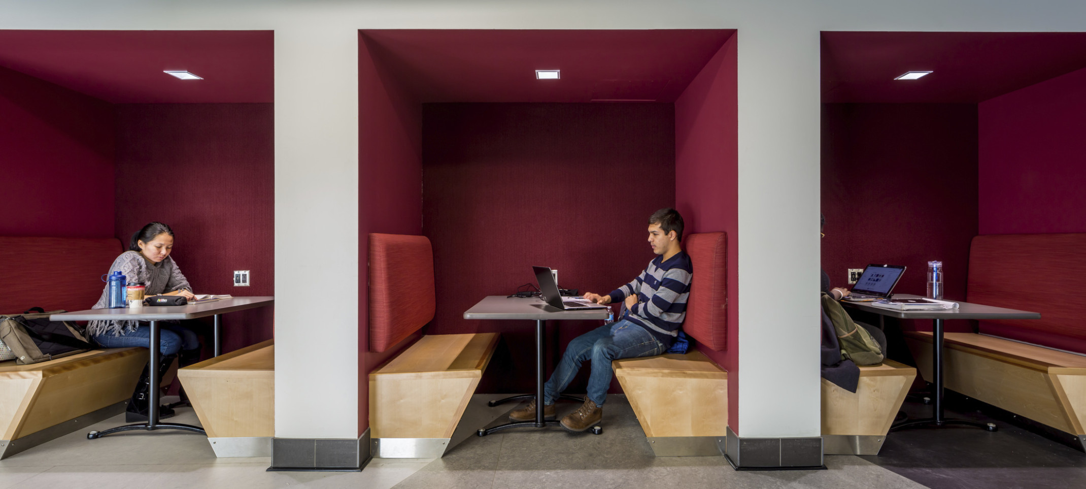 Tucked-in booths for collaboration with wood benches and dark red accents at the University of Minnesota cultural center