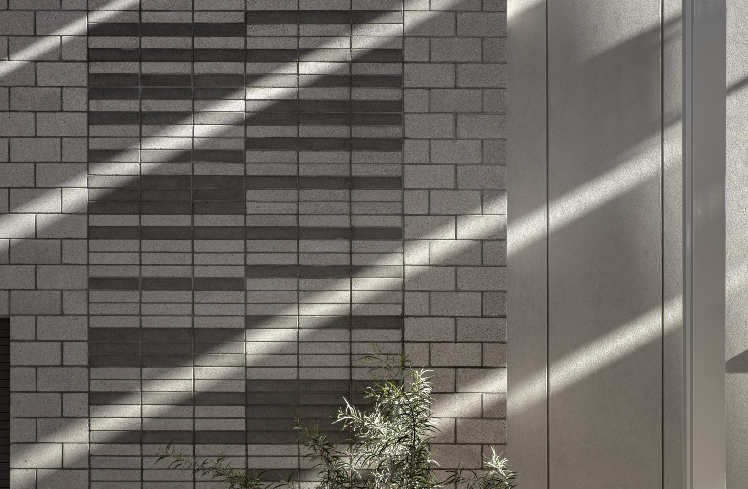 Stone wall at Canyon View High School with 2 sizes and color of stone. Stripes of shadow on wall, bush visible below